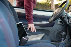 Losing laptops concept. Thief puts his hand through open car window to steal laptop from passenger seat