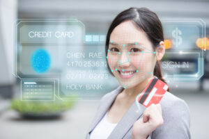 Biometrics payments concept. Smiling Asian woman holds up payment card while having face scanned
